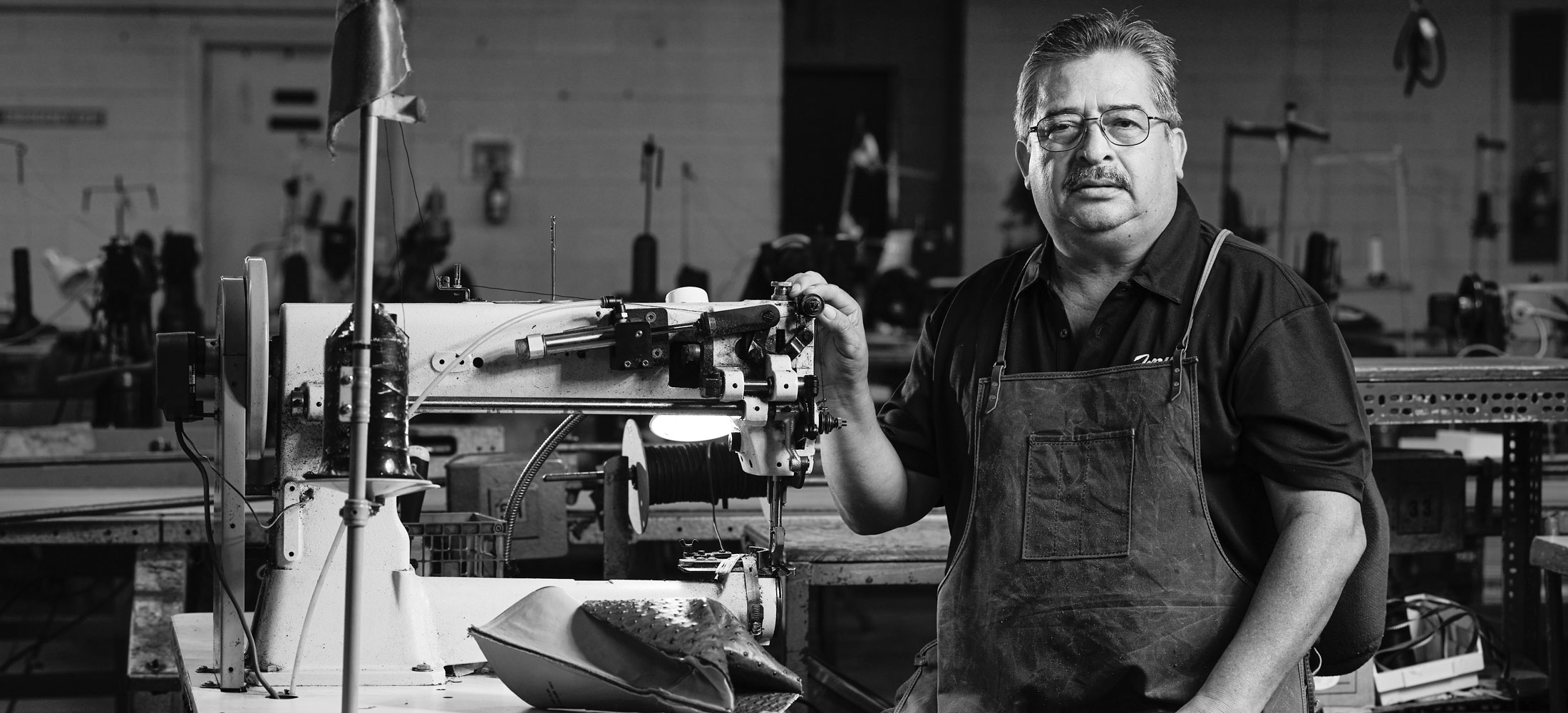 A Hispanic man wearing a polo shirt and an apron looks into the camera.